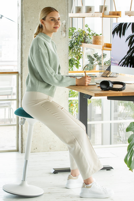 Frau sitzt auf ergonomischem Bürohocker am Ergotopia Schreibtisch